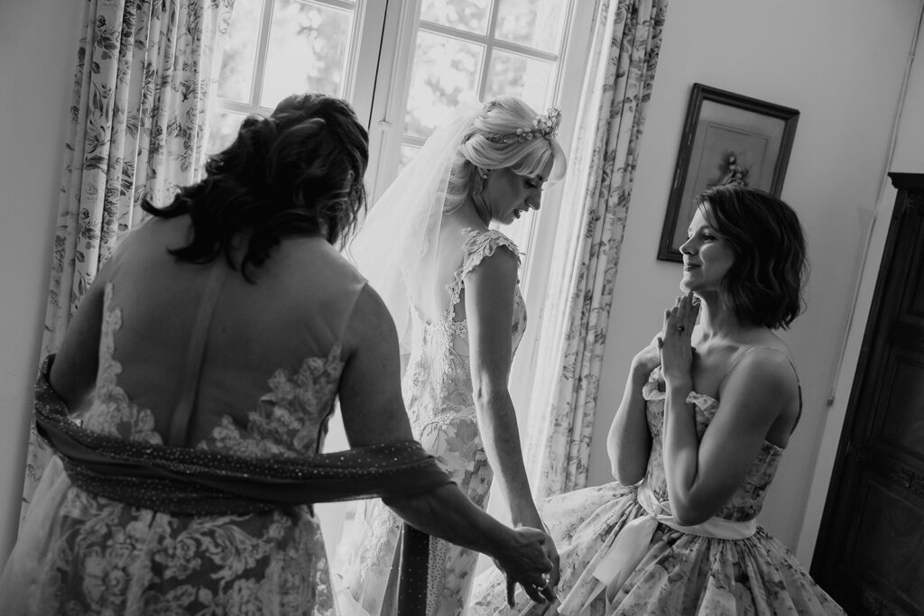 Black and white candid photo of bridesmaids helping the bride get ready. 