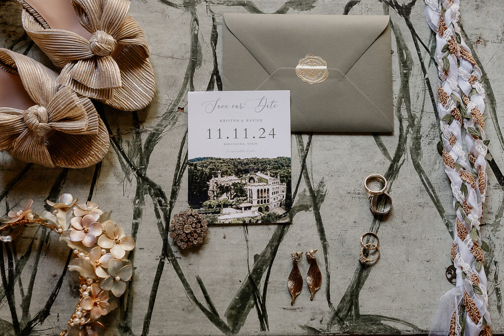Wedding detail flat lay with invitation, rings, hair accessories, and jewelry for a La Baronia wedding in Barcelona Spain.