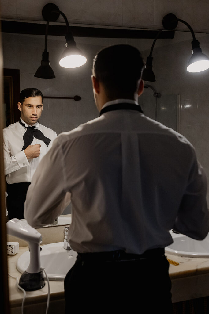 Groom adjusting his bow tie in the mirror while getting ready for a La Baronia wedding in Barcelona Spain.