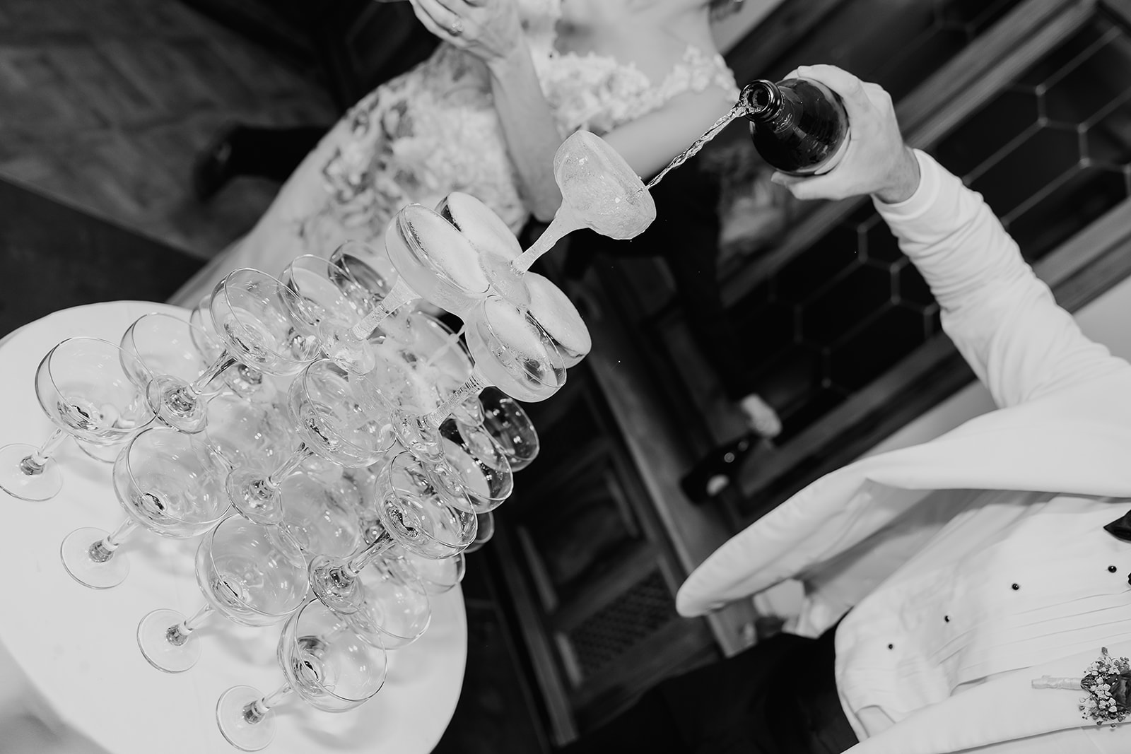 Black and white photo of a bride and groom pouring champagne into their champagne tower.