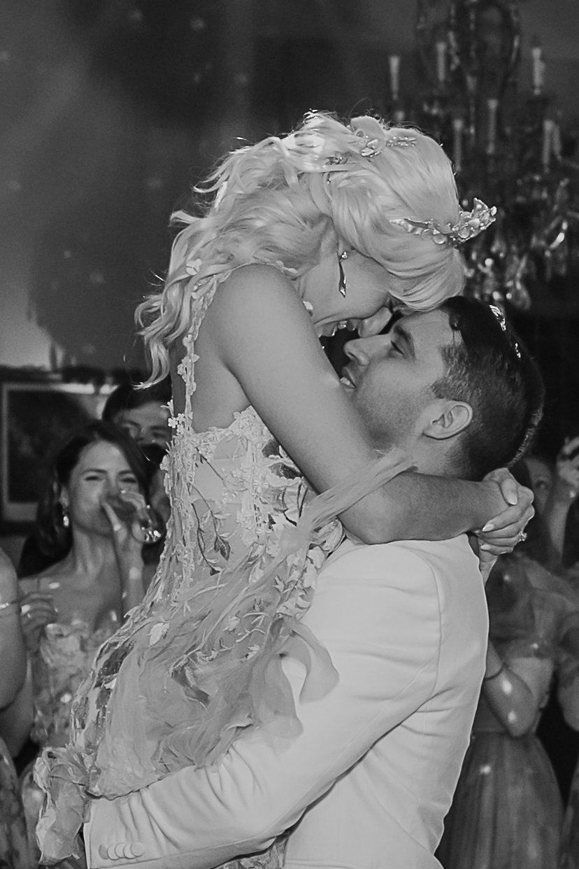 Black and white photo of a groom lifting up his bride during their wedding reception.