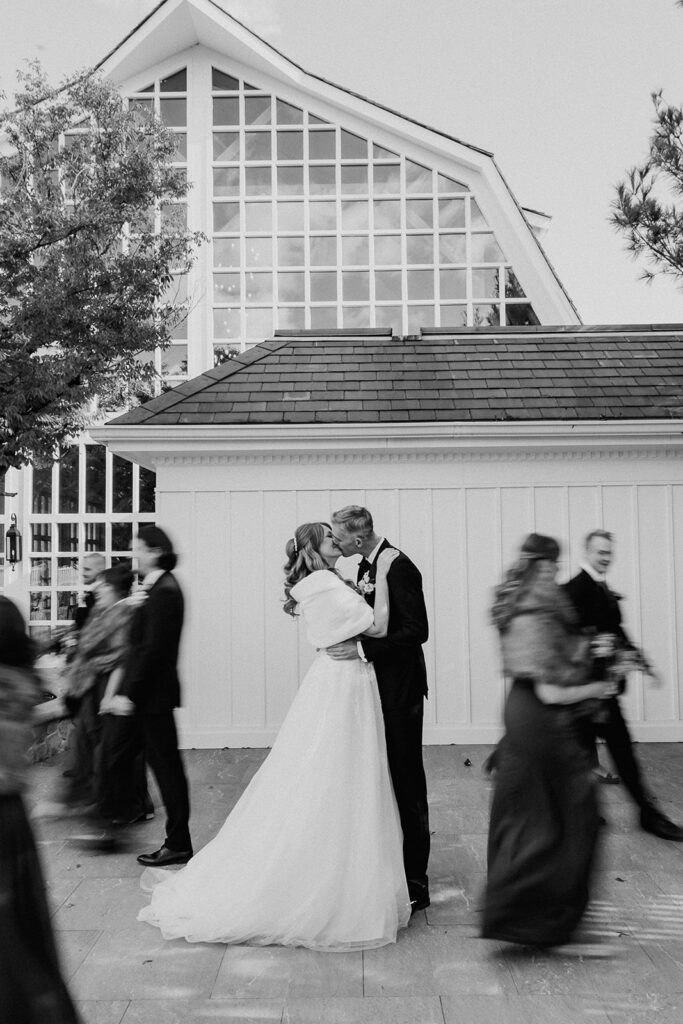 Bride and groom kissing while bridal party walks past in motion at The Farmhouse wedding venue in Hampton, NJ.