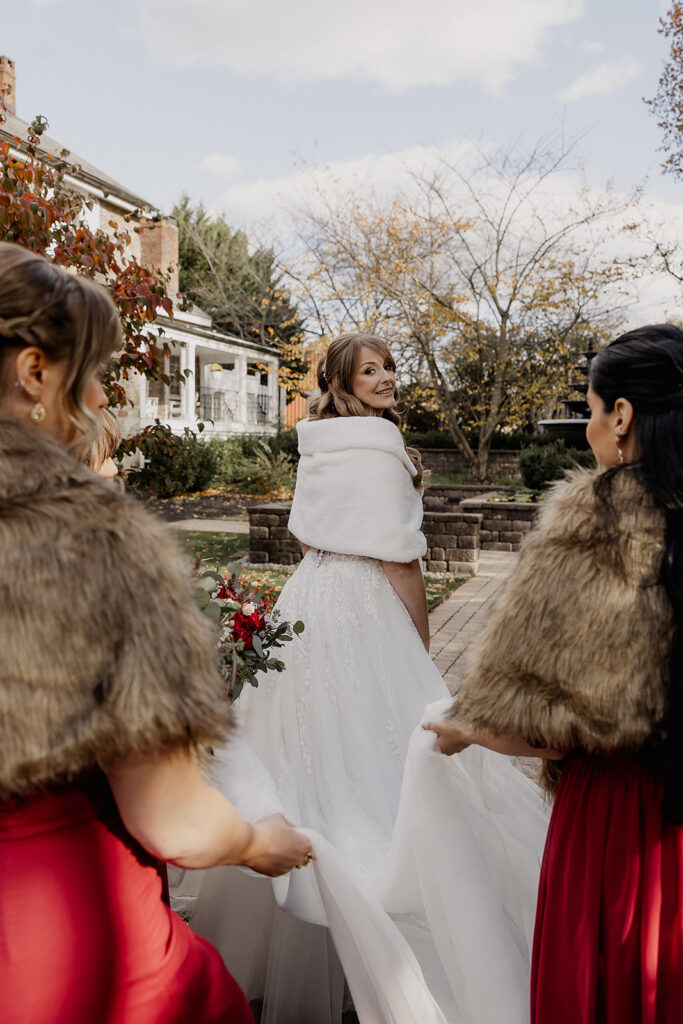 Bride walking while the bridesmaids hold her dress from behind at The Farmhouse wedding venue in Hampton, NJ.