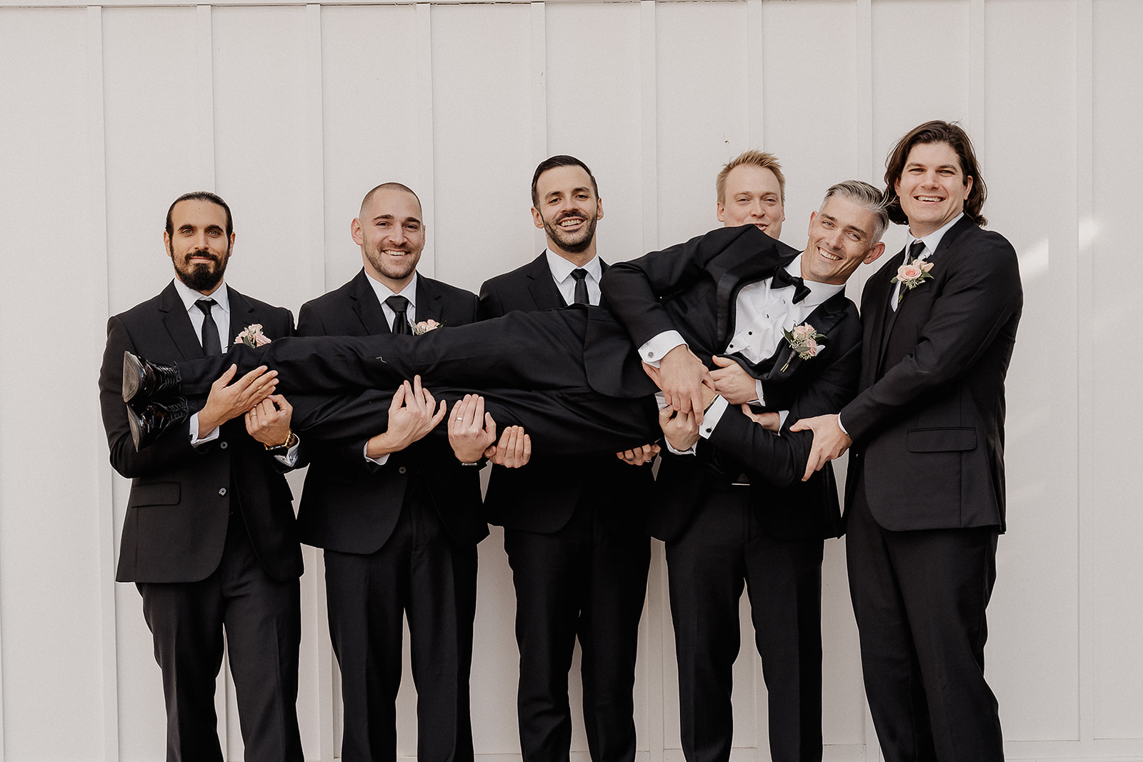 Groom lifted by groomsmen during bridal party portraits at The Farmhouse wedding venue in Hampton, NJ.