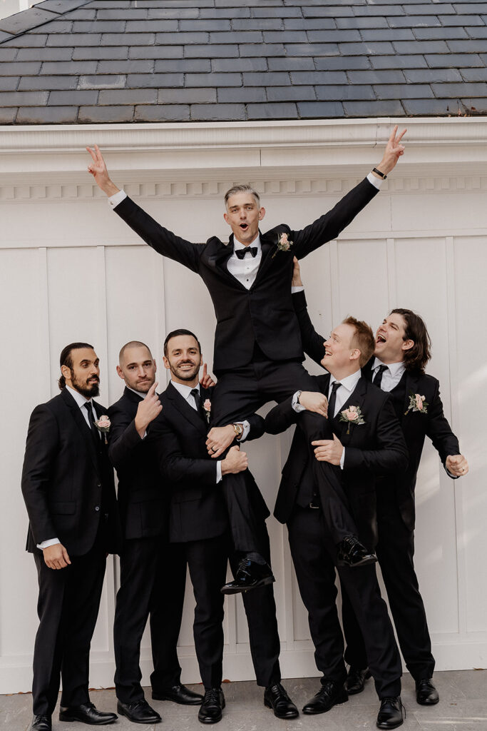 Groom lifted by groomsmen during bridal party portraits at The Farmhouse wedding venue in Hampton, NJ.