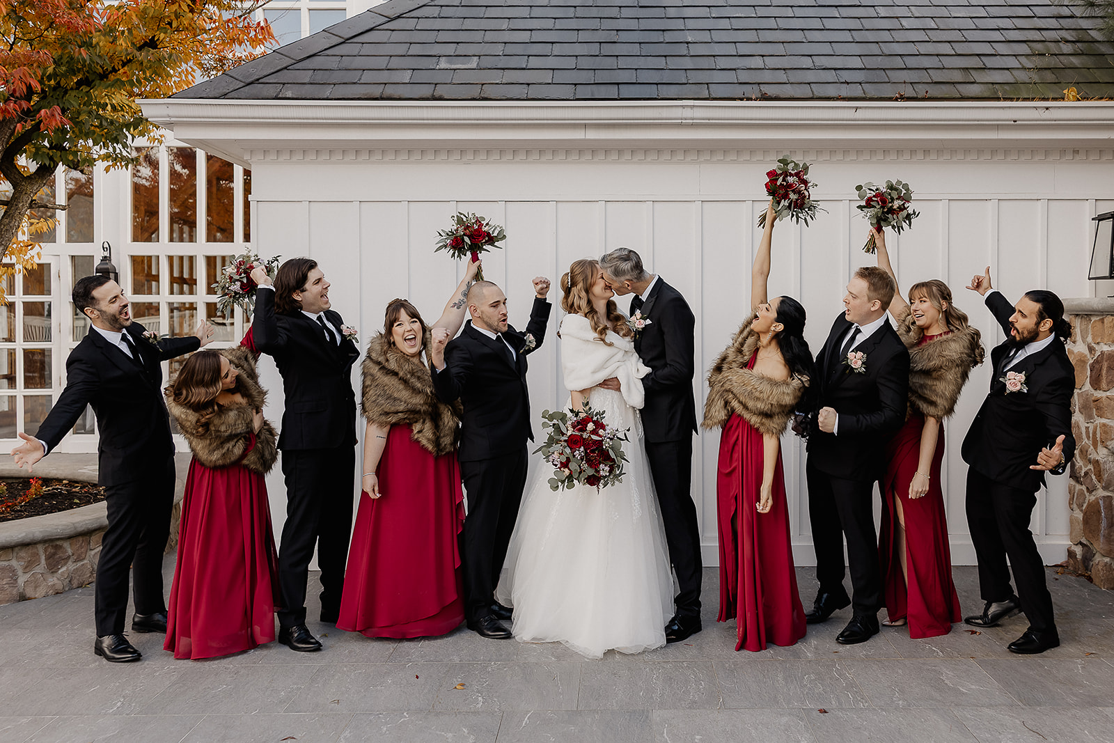 Bride and groom kissing surrounded by cheering bridal party at The Farmhouse wedding venue in Hampton, NJ.