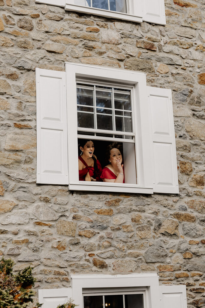 Bridesmaids watching the bride and groom share a first look from the farmhouse window.