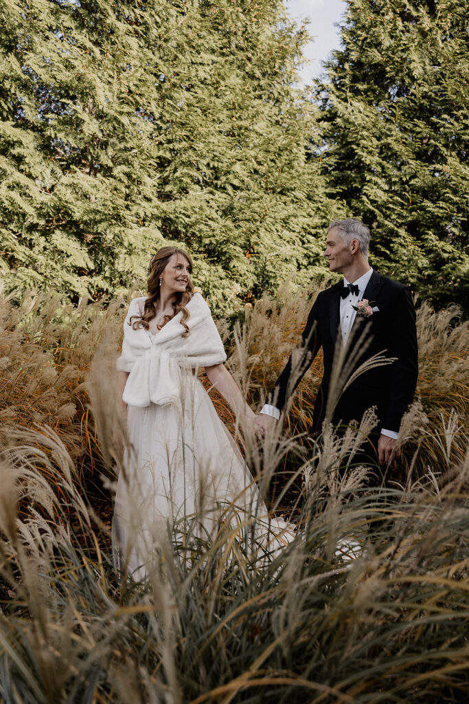 Bride and groom walking through tall grass during portraits at The Farmhouse wedding venue in Hampton, NJ.
