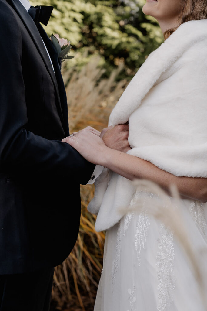 Close up shot of a bride and groom holding onto one another outdoors.