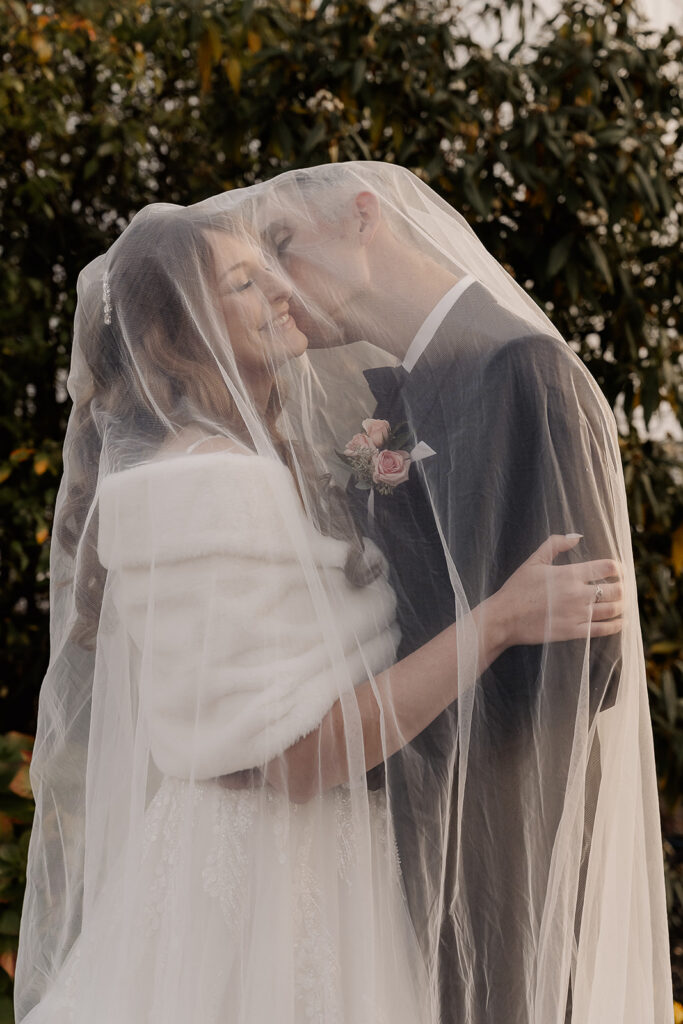 Groom kissing the bride with veil over them near at The Farmhouse wedding venue in Hampton, NJ.