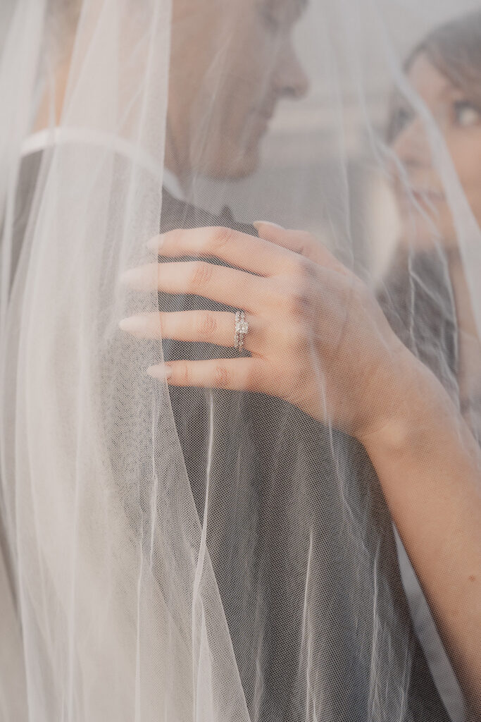 Bride and groom embracing with veil over them near silo at The Farmhouse wedding venue in Hampton, NJ.