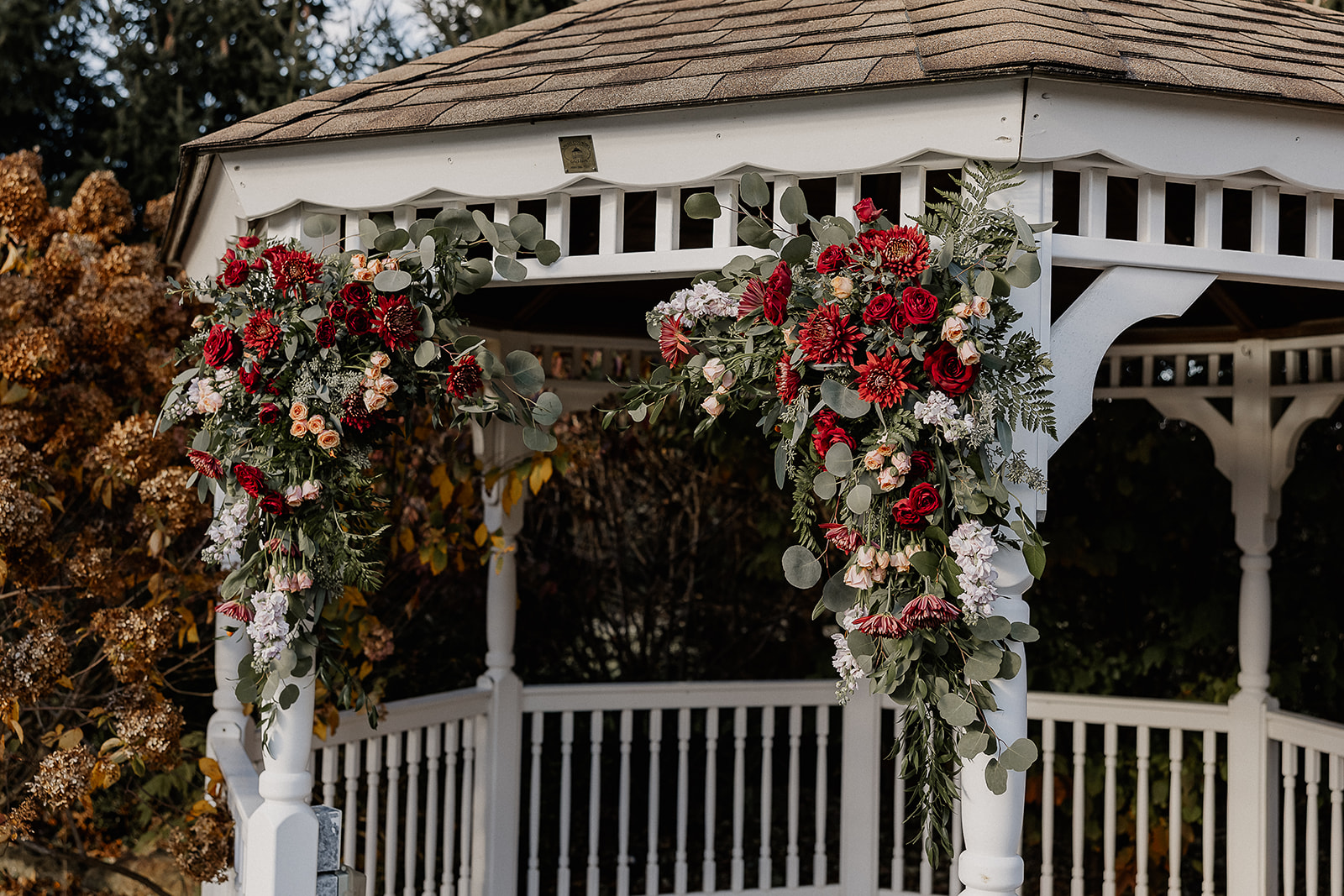 Floral ceremony arch with red and neutral flowers on gazebo at The Farmhouse wedding venue in Hampton, NJ.