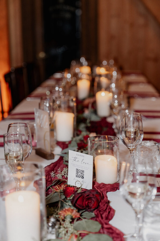 Reception table with candles, glassware, and red floral runner at The Farmhouse wedding venue in Hampton, NJ.