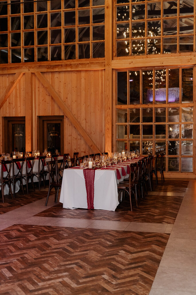 Wide view of indoor reception space with wood beams and long tables at The Farmhouse wedding venue in Hampton, NJ.