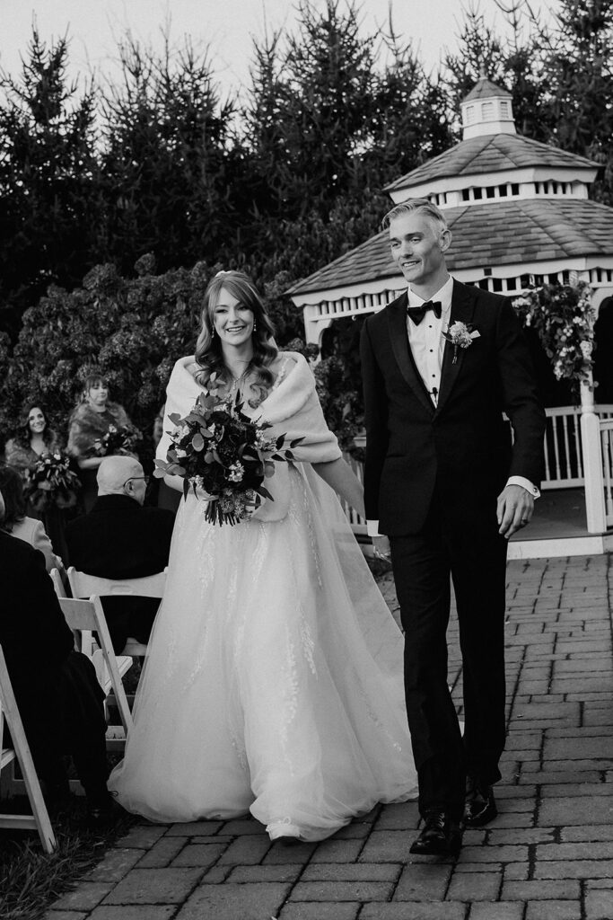 Black and white photo of a bride and groom walking back down the aisle as husband and wife after their ceremony.