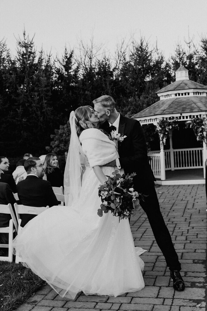 Black and white photo of a bride and groom kissing at the end of the aisle after their ceremony.