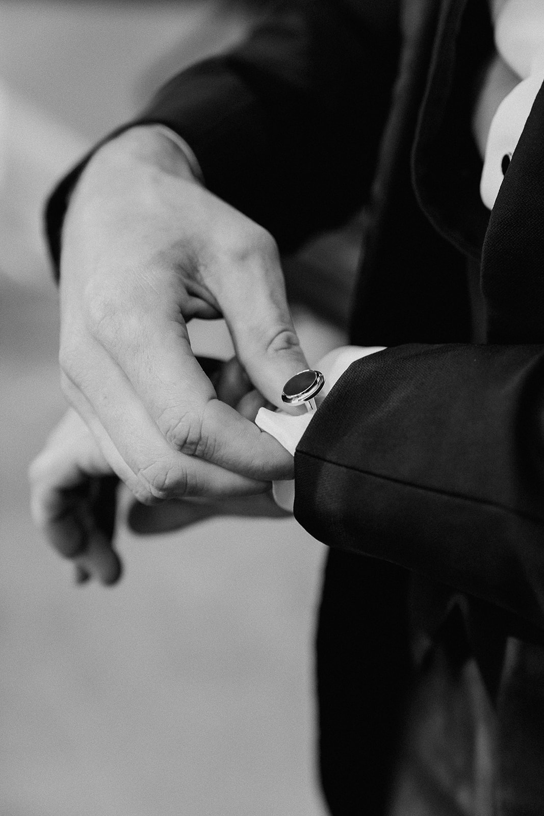 Black and white close up photo of a groom putting on his cufflinks.