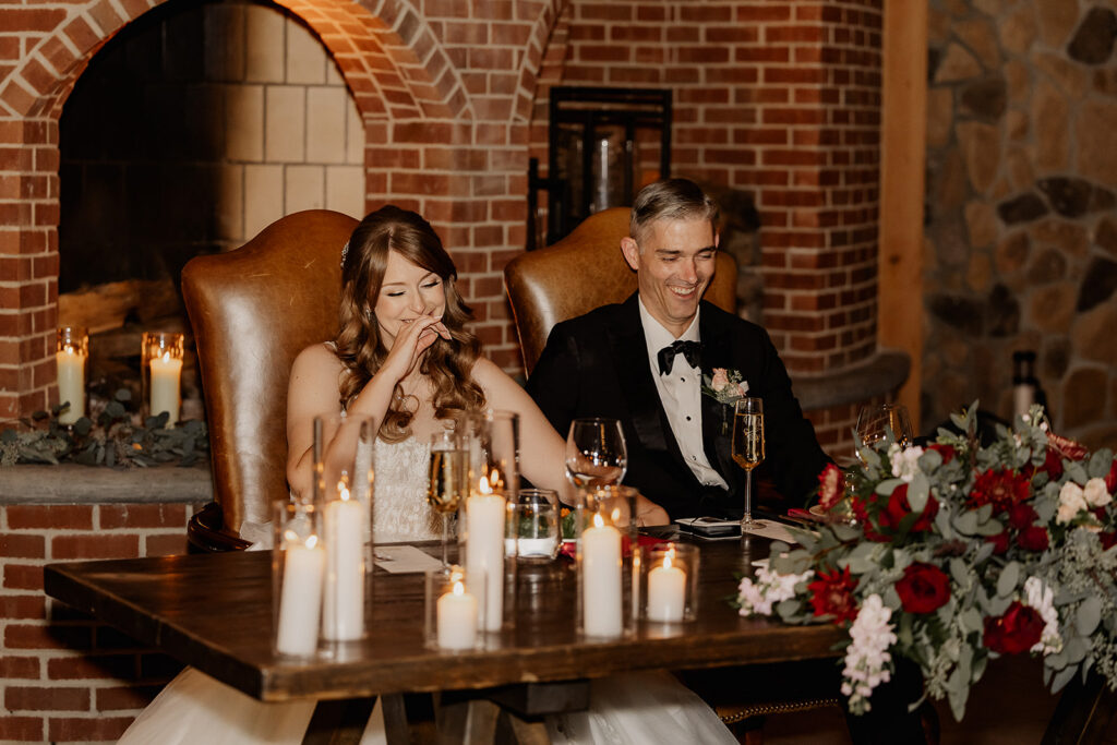 Bride and groom laughing during reception speeches.