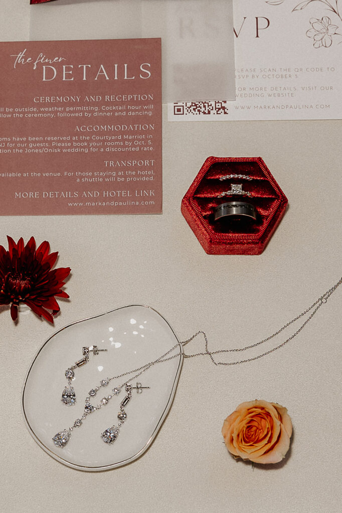 Flatlay detail shot of rings, jewelry, florals, and the details and RSVP.