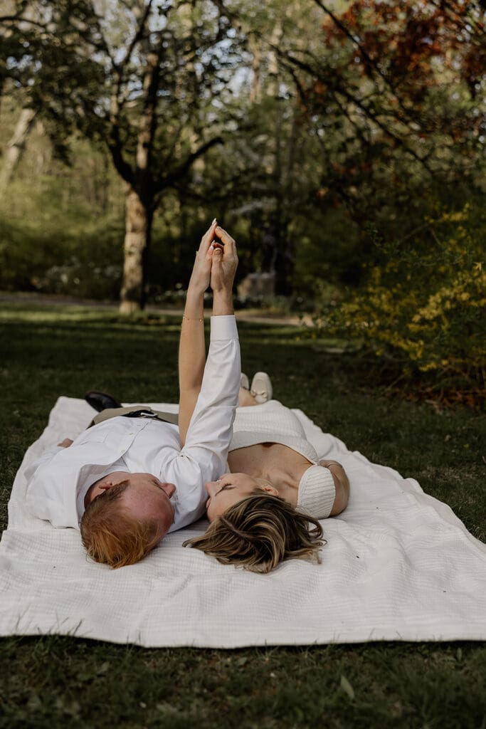 Couple laying on a blanket and holding hands during their Ringwood Botanical Gardens Engagement Photos in New Jersey.