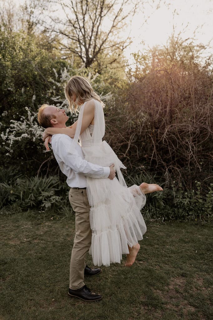 Man piking up his fiancé for their NJ engagement photos at Ringwood Botanical Gardens during golden hour.