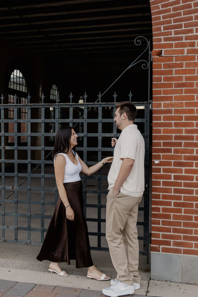 Couple posing in front of a gate and brick wall.