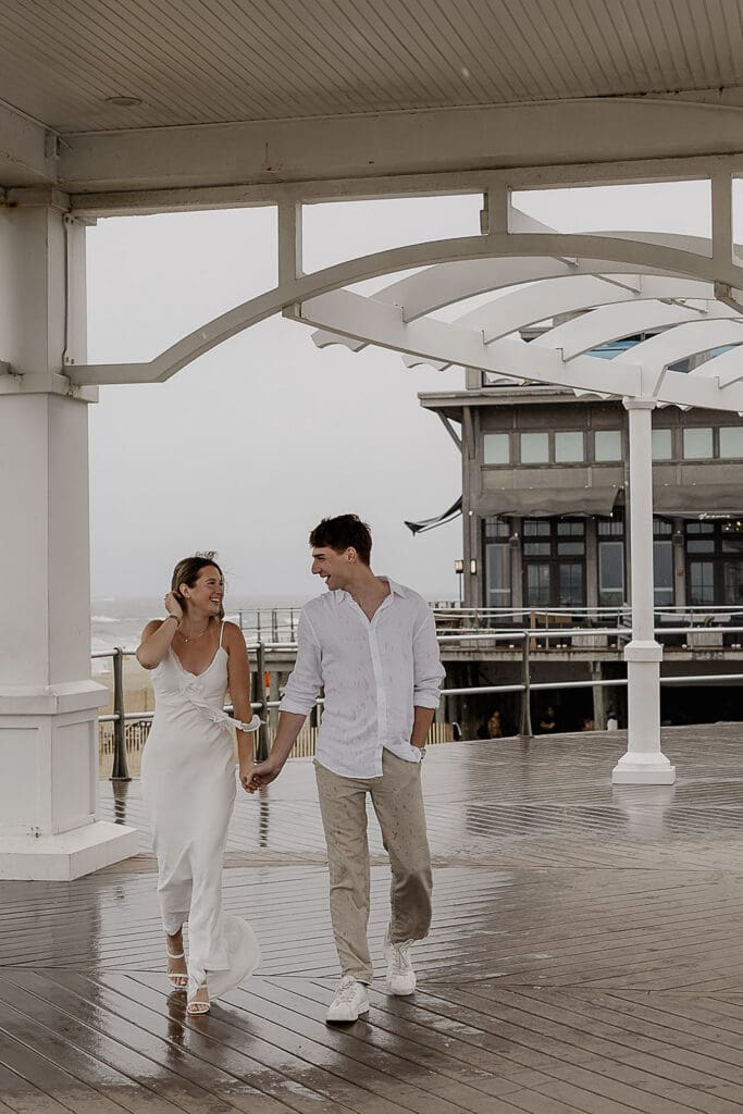 Couple holding hands and walking the boardwalk in Long Branch, NJ for their engagement session.
