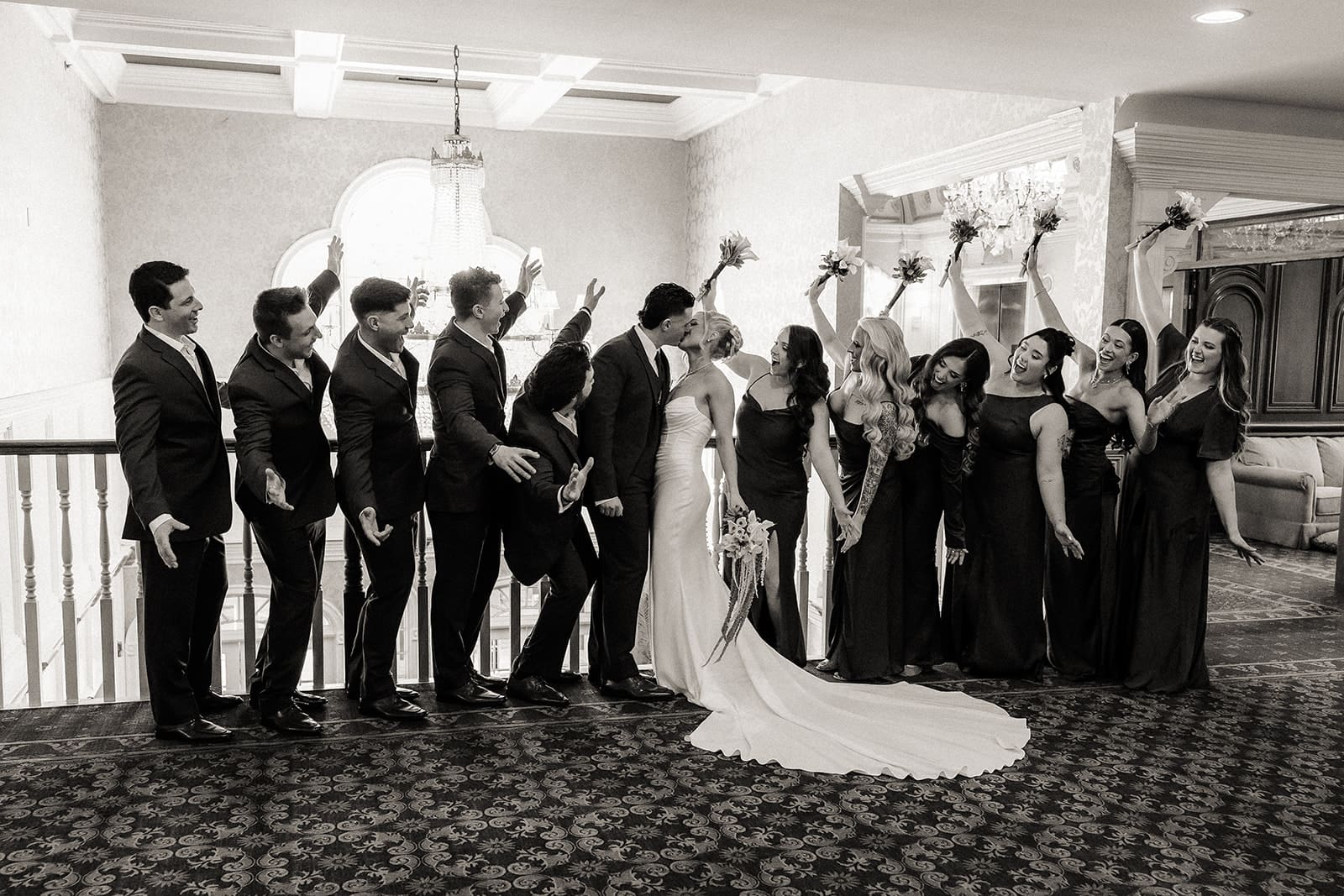 Bride and groom kissing with their wedding party cheering around them at The Brownstone in Paterson, NJ.