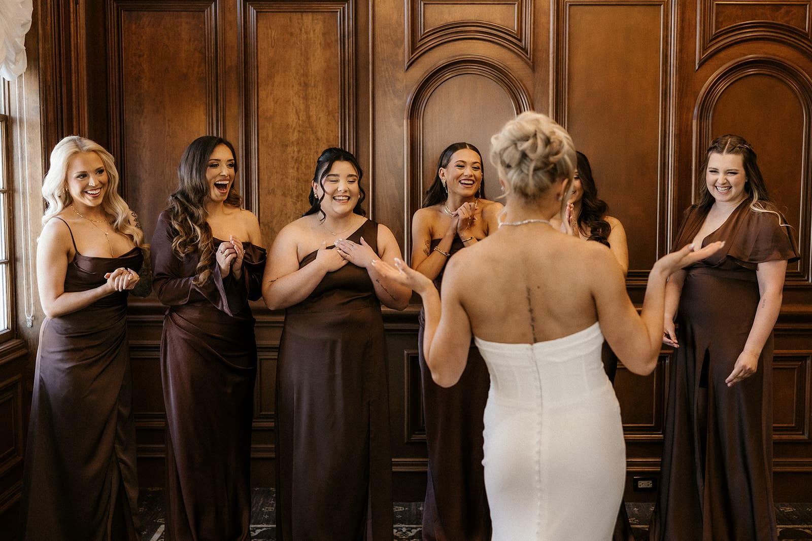 Bride sharing a first look with her bridesmaids at Brides dress hanging on the wall at The Brownstone in Paterson, NJ.