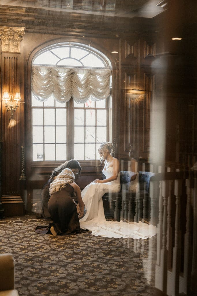 Bridesmaids helping bride get her wedding heels on.