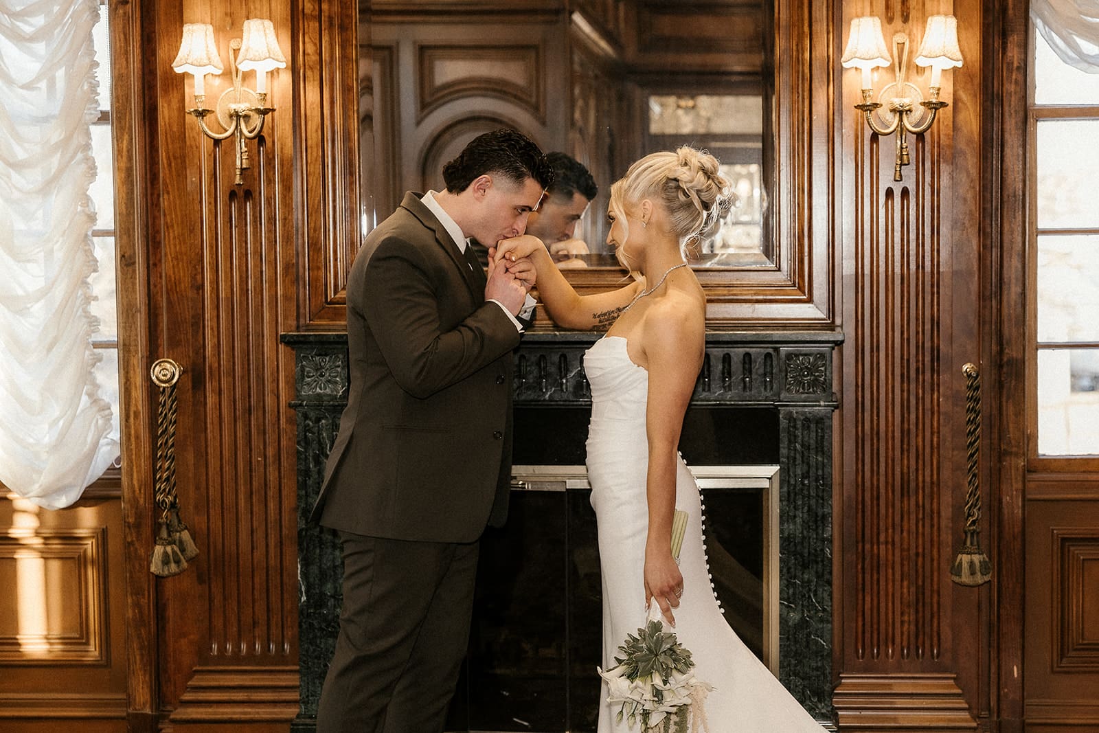 Groom kissing his brides hand by the fireplace inside The Brownstone in Paterson, NJ.