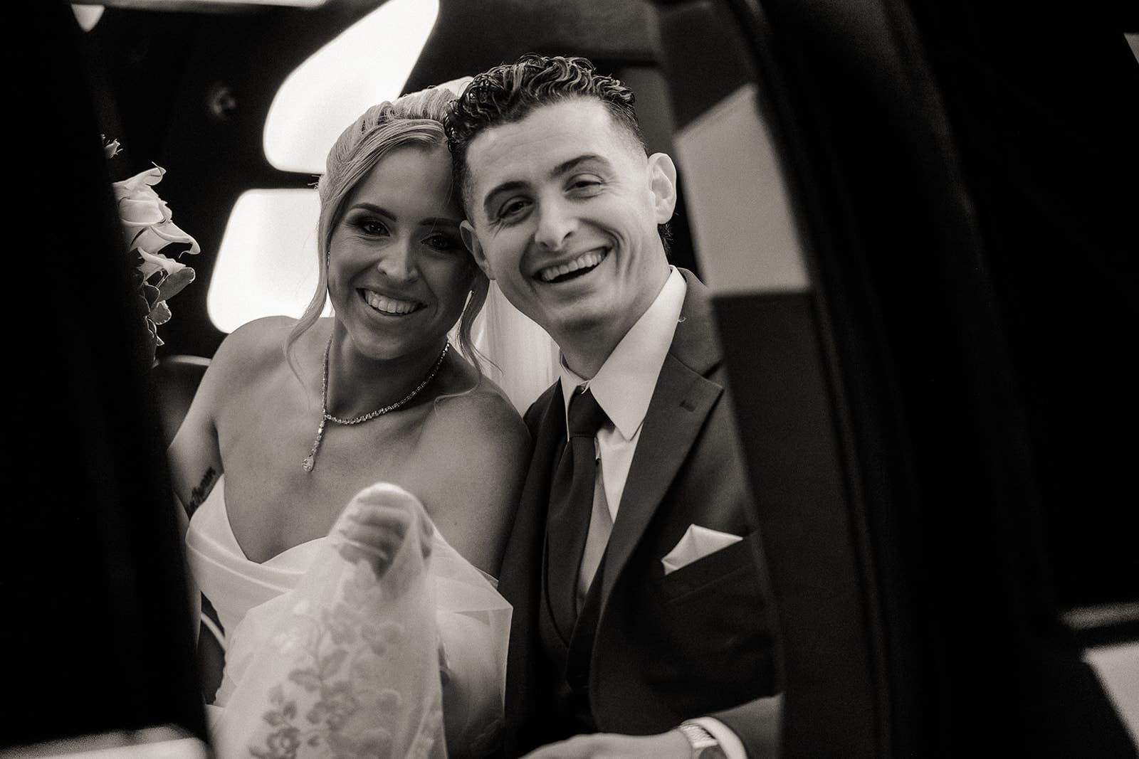 Black and white photo of a bride and groom smiling in their limo.