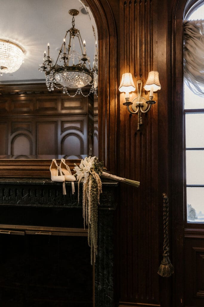 Brides heels and bouquet sitting on a fire mantle at Brides dress hanging on the wall at The Brownstone in Paterson, NJ.