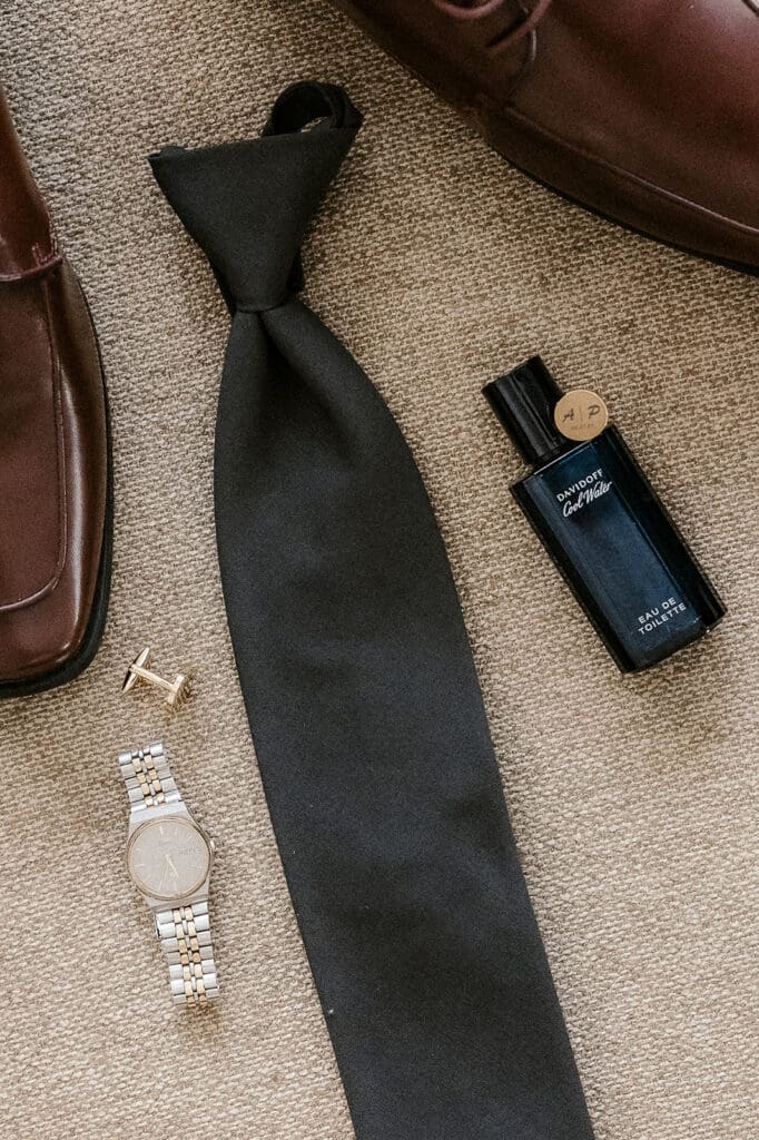 Grooms wedding details styled for a flatlay shot with his tie, cologne, custom cufflinks, shoes, and a watch. 