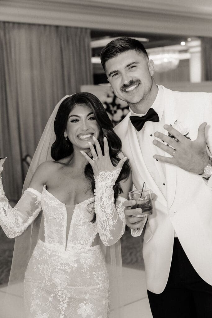 Black and white photo of the bride and groom showing off their rings during cocktail hour.
