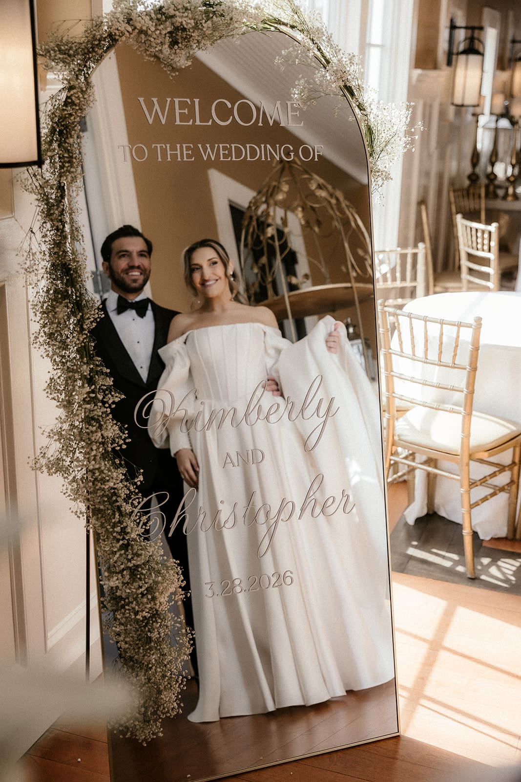 Bride and groom posing in the mirror that has their names and wedding date.