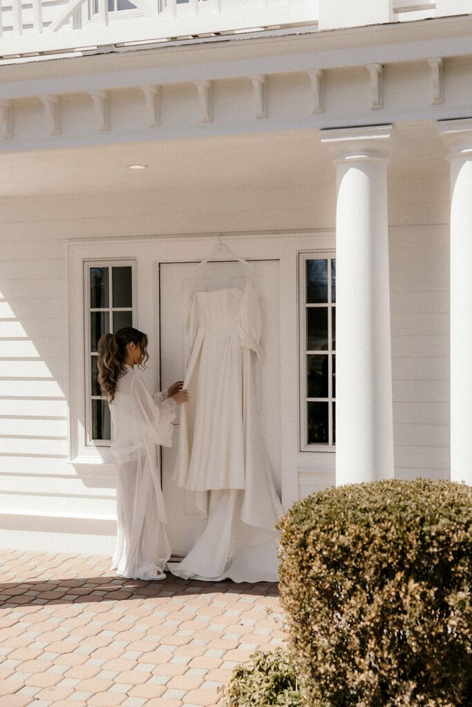 Bride admiring her dress hanging off the door.
