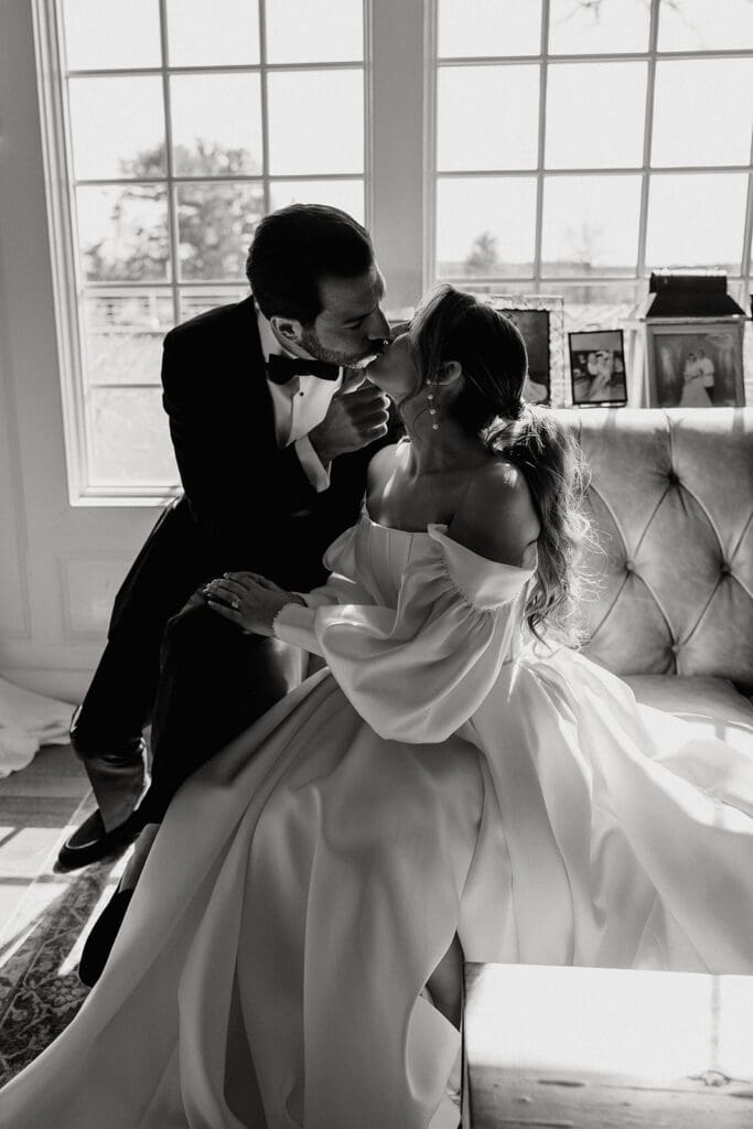 Black and white photo of a bride and groom kissing indoors.