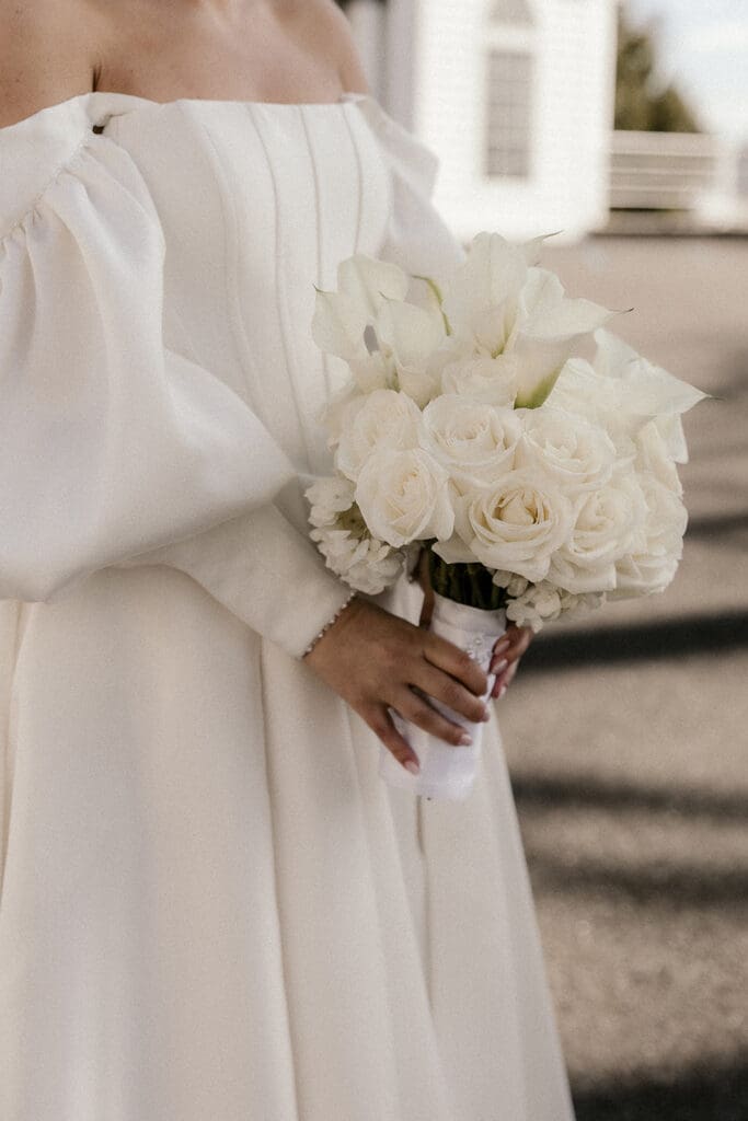 Close up photo of a bride holding a white wedding bouquet.