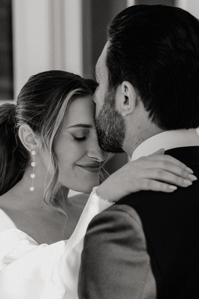 Black and white close up photo of a groom kissing his brides forehead.