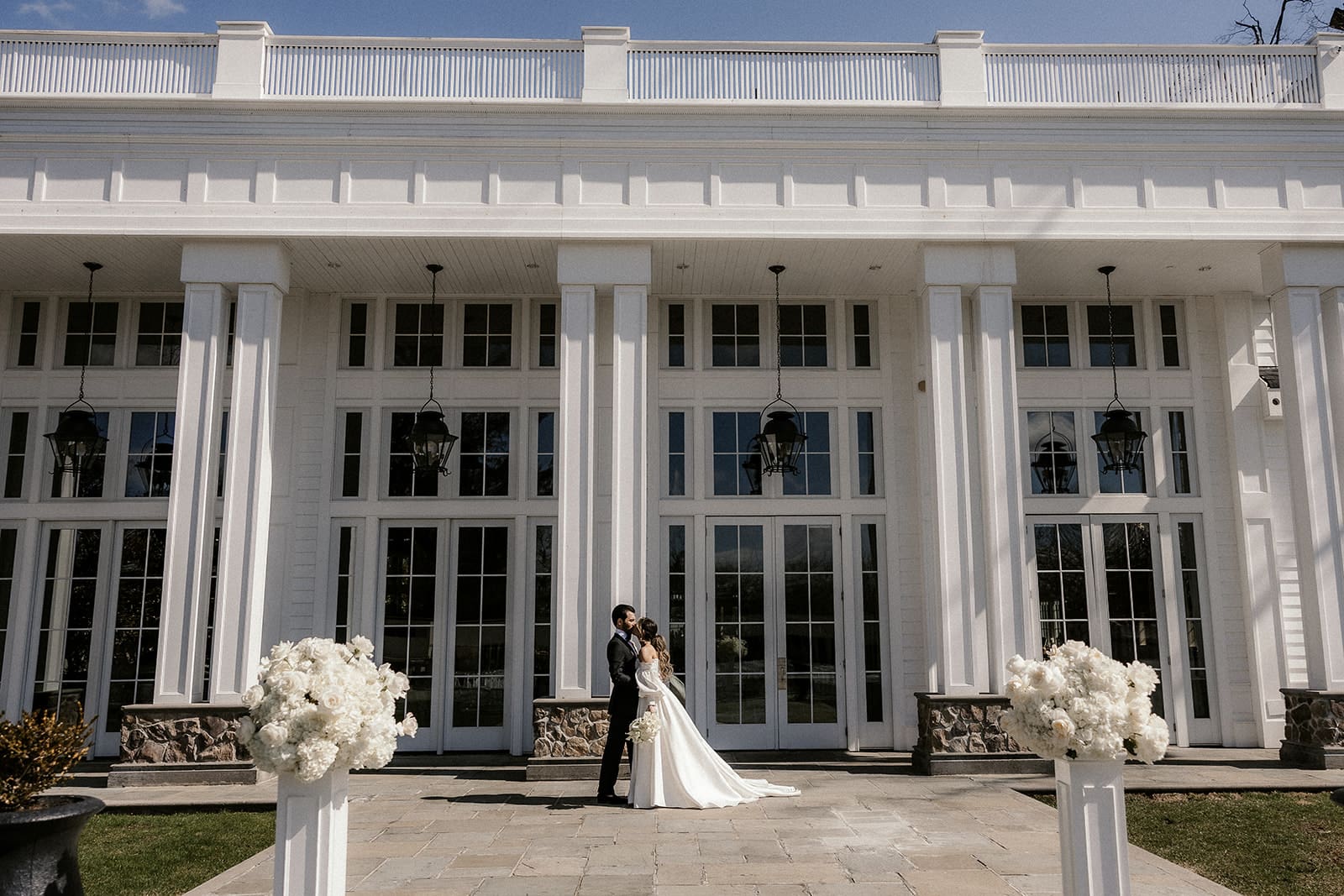 Wide outdoor shot of a bride and groom kissing in front of The Rylan Inn in White House Station, NJ.