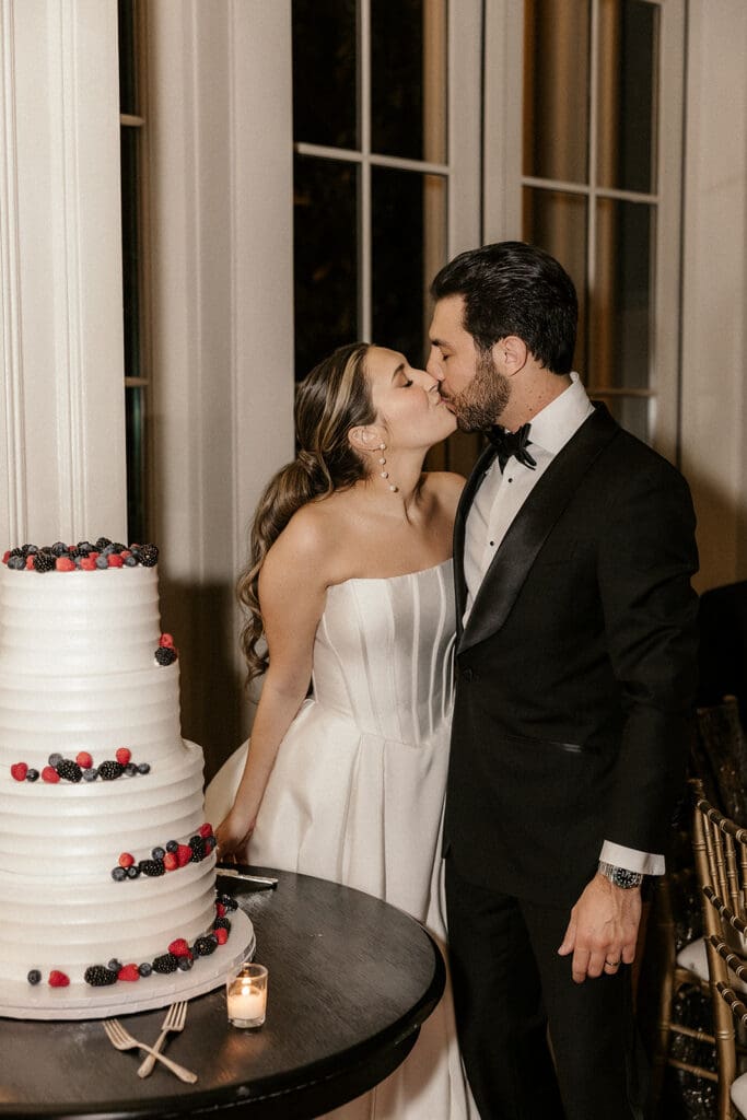 Bride and groom kissing next to their four-tiered wedding cake.