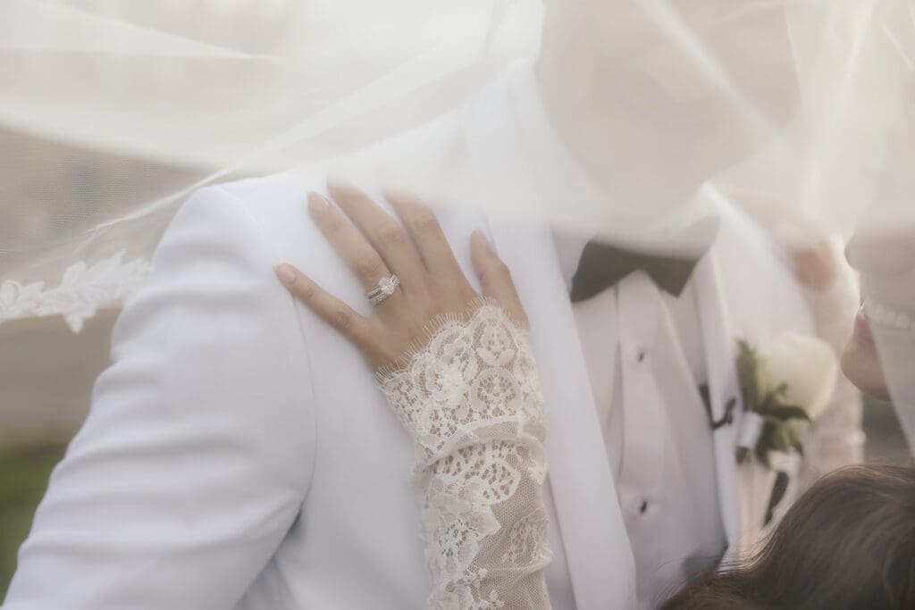 Wide shot of a bride and groom posing under her veil for their portraits.