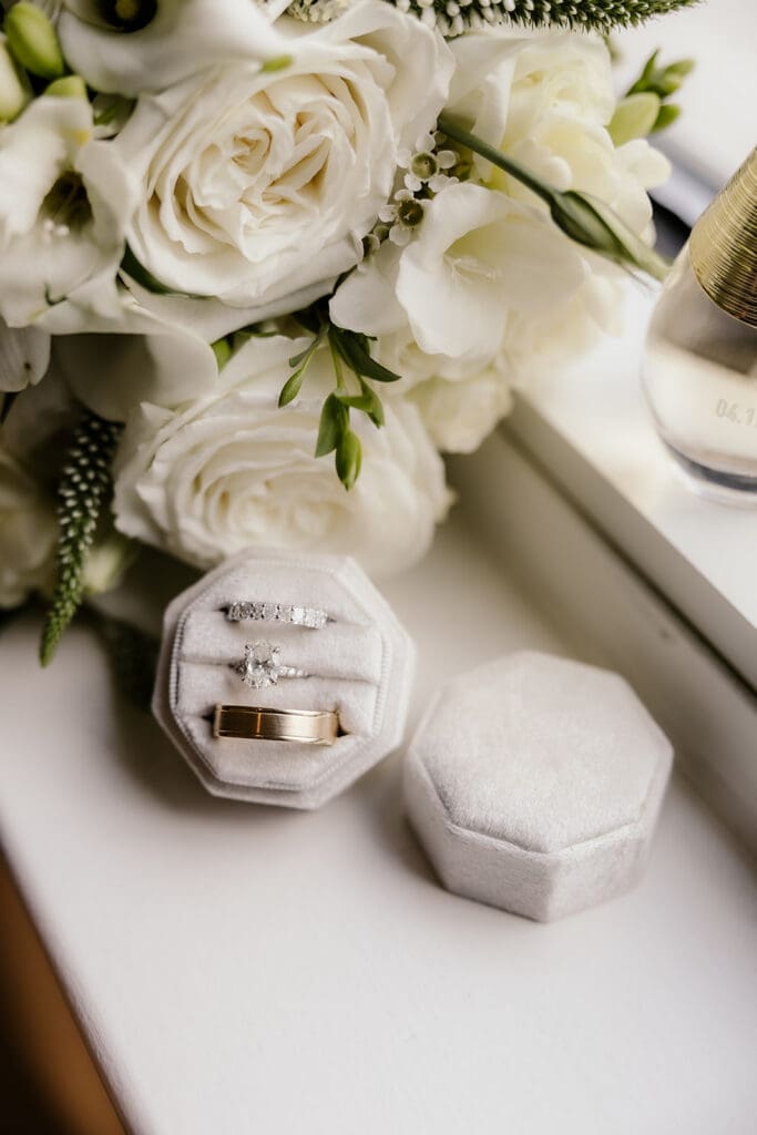 Detail shot of rings and wedding band in a ring box next to florals.