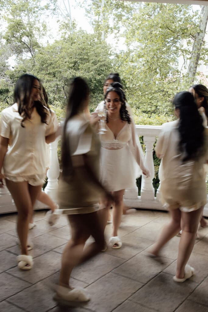 Motion blur photo of bridesmaids walking around the bride on the balcony off of The Bridal Suite with glasses of champagne.