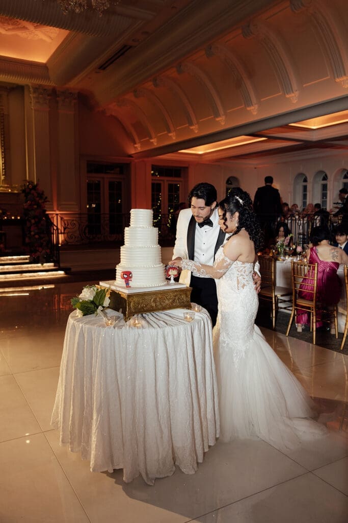 Bride and groom cutting into their four-tiered white wedding cake.