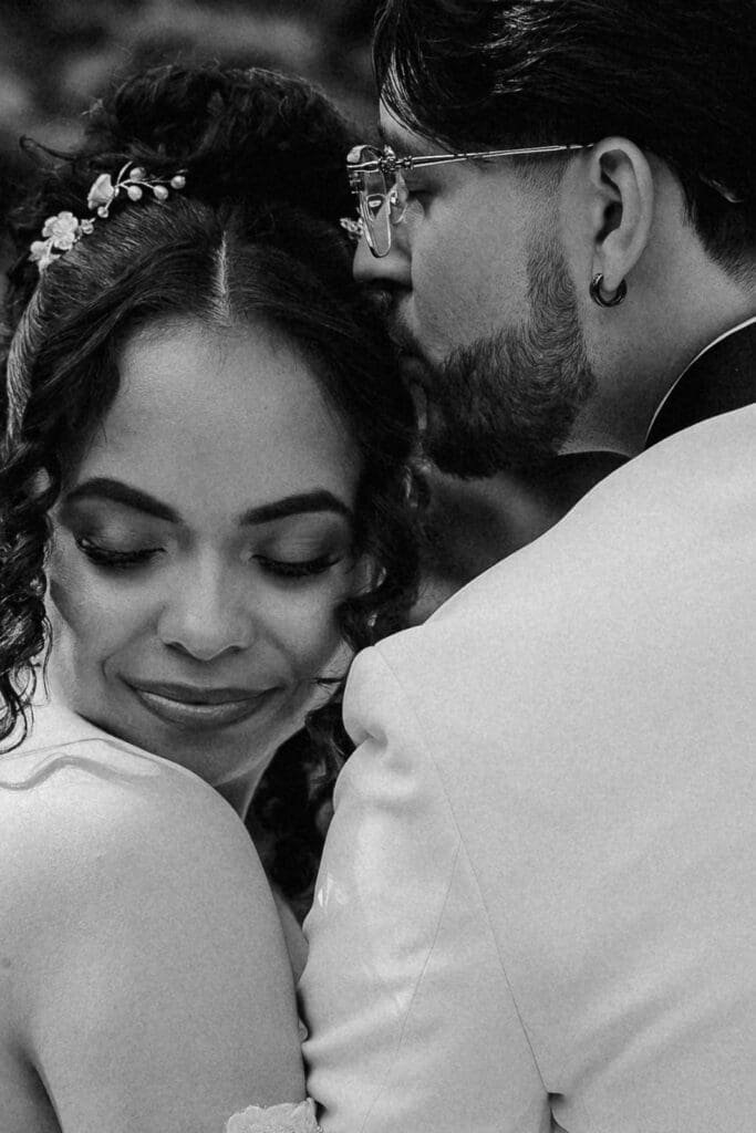 Close up black and white portrait of a groom kissing his bride on her head.