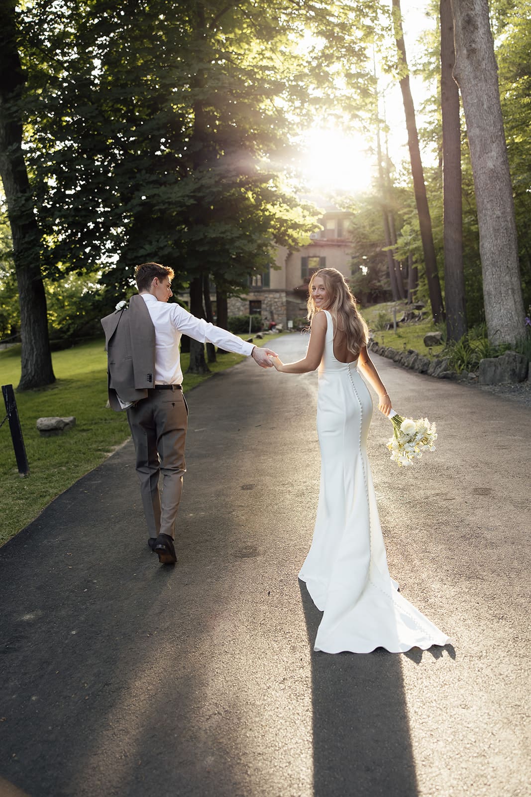 Bride and groom walking up the long driveway at Arrow Park wedding venue during golden hour.