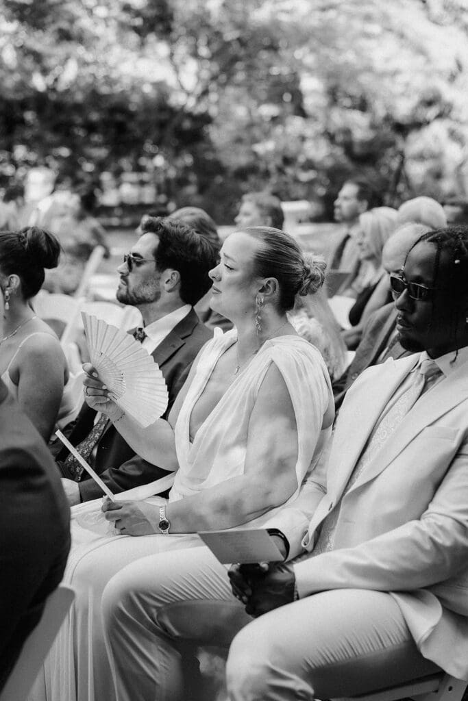 Black and white candid photo of guests watching a wedding ceremony.