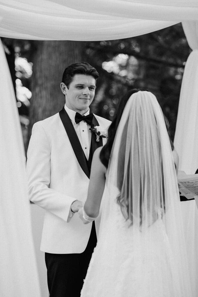 Black and white photo of a bride and groom holding hands during their ceremony.